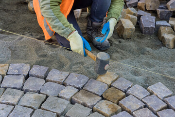 Close-up of construction worker installing laying pavement stones on sidewalk near road