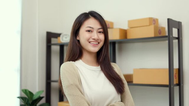 Beautiful young asian entrepreneur standing pose smiling to camera. Female small Business owner working at home. Startup freelance people with many parcel on background.