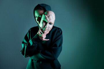 Hiding behind a mask, a young woman in a dark hoodie hides her face with a mask, privacy on the...