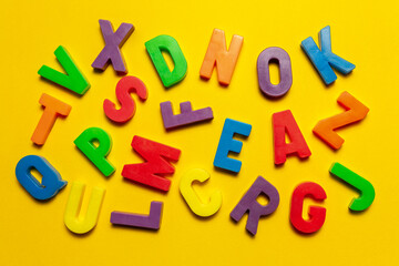 Plastic magnetic letters and numbers isolated on yellow, top view. Dyslexia and language disorders