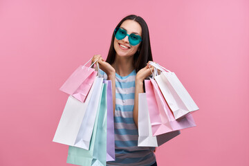 Portrait of beautiful happy smiling girl holding posng with many shopping bags in hands isolated over pastel pink background