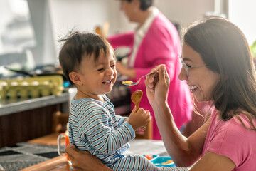 Latin baby boy having fun with his mother during breakfast smiling