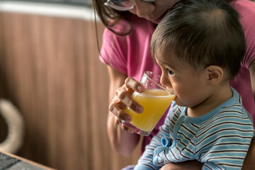 Latin baby boy zipping orange juice for breakfast in the kitchen