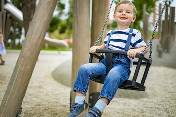 Smiling boy riding on swing at amusement forest park or childish playground having positive emotion