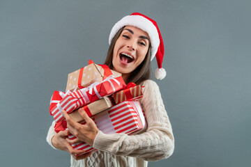 Portrait of excited smiling girl in Santa's hat holding a big pile of present boxes in hands,...