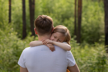 Caucasian daughter in the arms of dad and hugs him looking at the camera