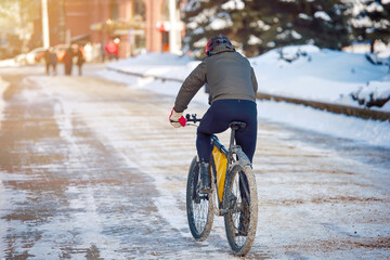 Male cyclist on snowy, slippery pathway after snow storm. Man cycling in winter city street. Man in...