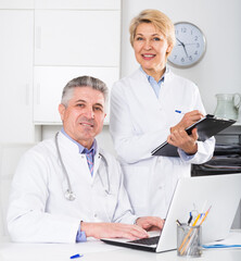 Mature doctor and nurse in white medical gown waiting for patients visit