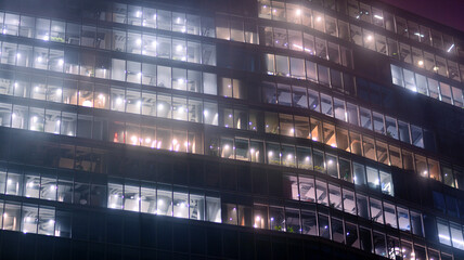 Corporate building at night - business concept. Glass wall office building .Modern office windows of skyscraper glowing at night. - obrazy, fototapety, plakaty