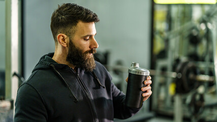 Front view portrait of young caucasian man athlete in black hoodie male standing in the gym holding...