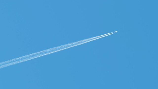 Distant passenger jet plane flying on high altitude on clear blue sky leaving white smoke trace of contrail behind. Air transportation concept