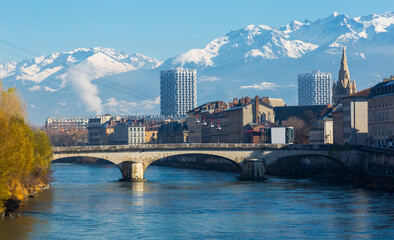 Naklejka premium Cityscape of Grenoble with famous cable car against backdrop of snowy Alps in sunny day, France