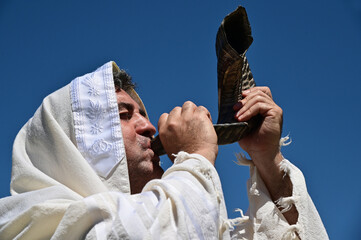 Portrait of an orthodox adult Jewish man blow Shofar (ram's horn) outdoors under clear blue sky, on...