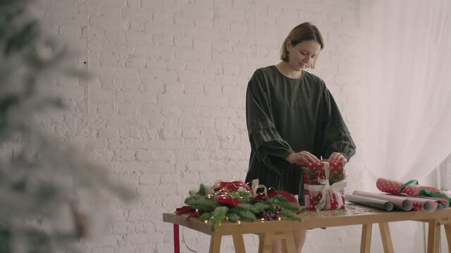 Portrait of a girl decorator of a gift wrapper standing at a table with decorations with gift wrapping paper, Christmas branches and ribbons