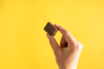 Close up on hand of unknown caucasian woman holding sweet brown chocolate cube above yellow...