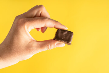 Close up on hand of unknown caucasian woman holding sweet brown chocolate cube above yellow...