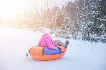 A cheerful girl in warm clothes rides down snowy hill on slide-slide cheesecake