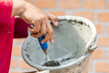 Fototapeta na wymiar Close up hand of worker holding trowel and bucket with fresh cement, Construction bricklayer worker building walls with bricks, mortar and putty knife
