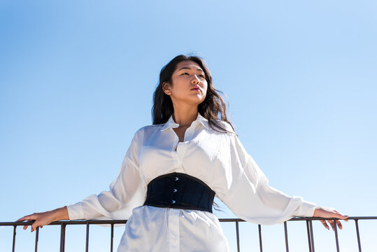 Asian woman leaning on a railing. Blue sky background.