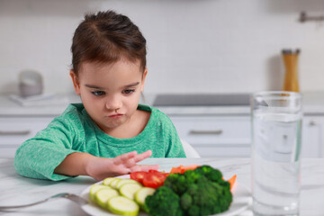 Cute little girl refusing to eat vegetables in kitchen