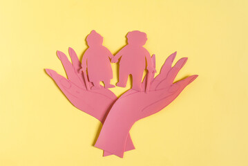 Obraz premium Cardboard figurines open palms of hands hold two elderly people. The concept of protecting the elderly and pensioners