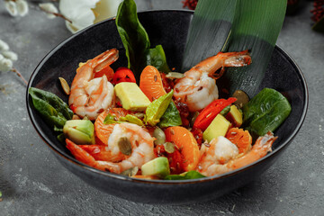 Shrimps salad with cherry tomatoes, cucumeber, avocado, lettuce and pomegranate on dish. Healthy seafood concept. Tasty grilled prawn shrimp and mix vegetable salad on black, top view