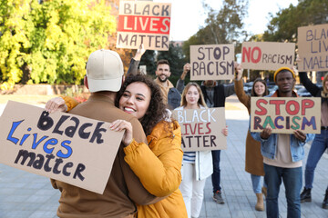 African American woman hugging man and holding sign with phrase Black Lives Matter outdoors during...