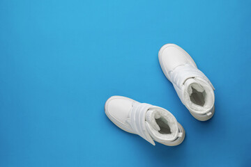 Top view of a pair of white women's sports shoes on a blue background. Flat lay. Place for text.