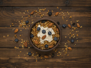 Muesli and yogurt in a deep clay bowl on a wooden table. Flat lay. Place for text.