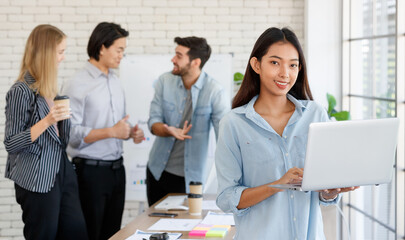 Cheerful Asian woman browsing laptop near multiethnic colleagues