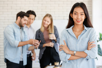 Positive Asian female manager standing near group of multiracial coworkers discussing project while working together in light conference room