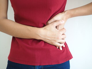 Woman wearing red t shirt on a white background hold hands on his stomach, liver pain, pancreas, kidneys problems. closeup photo, blurred.