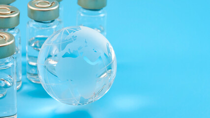 Global vaccines supply, international medical emergency and worldwide vaccination effort concept with glass globe and vaccine doses isolated on blue background with copy space