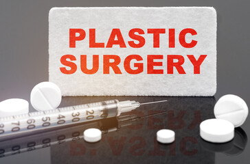 On a black reflective surface, pills, a syringe and a sign with the inscription - PLASTIC SURGERY
