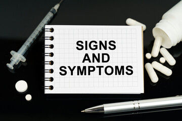 On the black surface are pills, a syringe and a notebook with the inscription - SIGNS AND SYMPTOMS