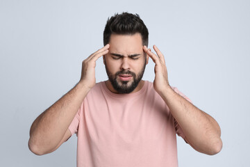 Young man suffering from headache on light background