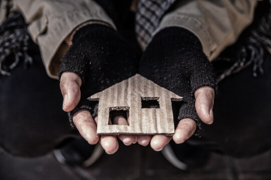 House shaped cardboard on dirty hands of homeless beggar.