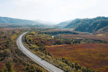 Fototapeta premium Mountain road and winding river in mountains gorge, autumn landscape, red leaves, aerial drone view