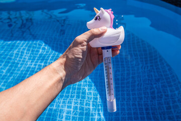 Checking the temperature of the swimming pool water with a funny thermometer. Unicorn pool thermometer