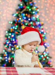 Pensive little girl wearing red christmas hat writes letter to Santa Claus
