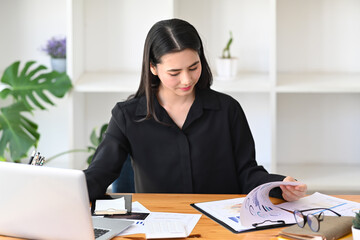 Attractive businesswoman reading documents and working with laptop computer.