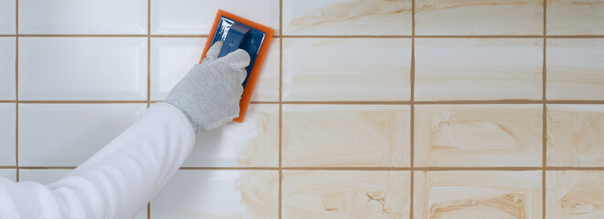 close-up of the process of grouting cracks, on the wall tiles with a spatula with foam, there is a...