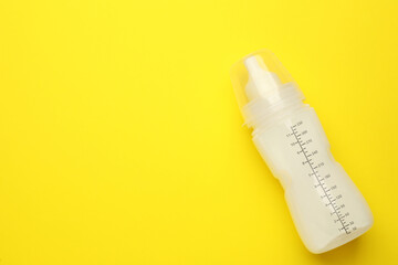 Feeding bottle with infant formula on yellow background, top view. Space for text