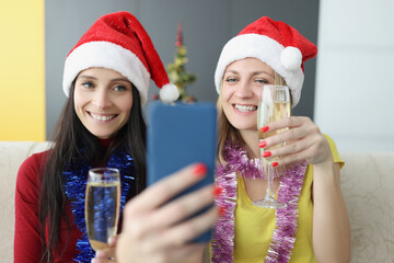 Obraz premium Cheerful sisters making selfie on smartphone holding champagne glasses
