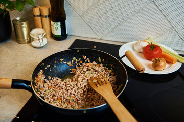 Close up of cooking bolognese sauce in pan on induction stove in the kitchen