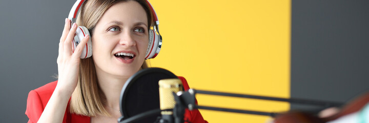 Woman singer in headphones singing song into microphone in recording studio