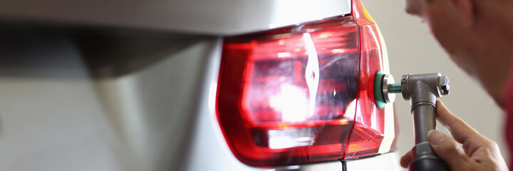 Man repairman polishing car headlights with machine in workshop closeup