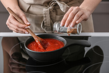Woman cooking organic tomato sauce in frying pan on stove in kitchen