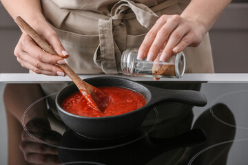 Woman cooking organic tomato sauce in frying pan on stove in kitchen