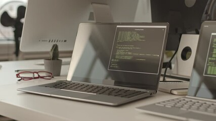 Close-up of two laptops with running program codes on screens at modern programmers office